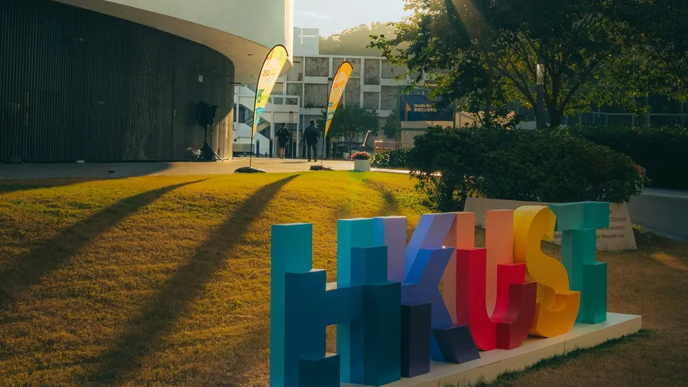 Colorful HKUST letter sign on the university lawn at sunset.
