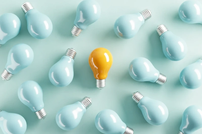 A yellow idea bulb among pale blue light bulbs.